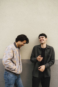 Multi-ethnic male friends laughing while talking with each other against beige wall