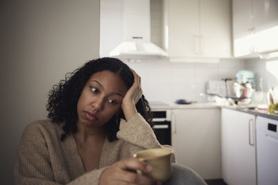 Pensive young woman sitting at home