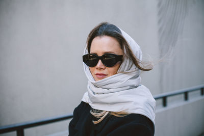 Portrait of woman wearing sunglasses standing against wall