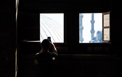 Rear view of man photographing through window