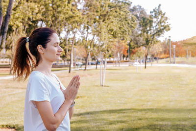 Side view of young woman standing against trees