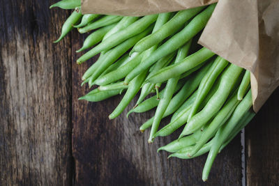 High angle view of green beans with wax paper on wooden table