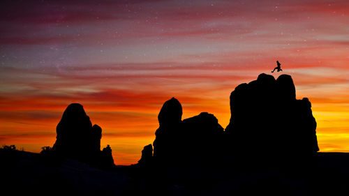 Silhouette man on rock against sky during sunset