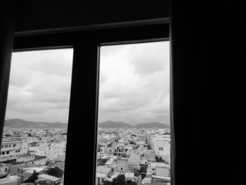 Buildings in city against cloudy sky seen through window