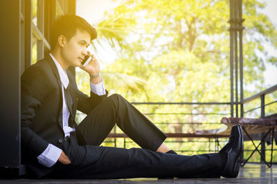 Young man using phone while sitting on window