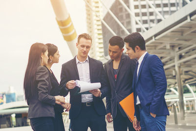 Business colleagues discussing while standing on footpath in city