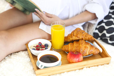 Midsection of woman with breakfast sitting on bed