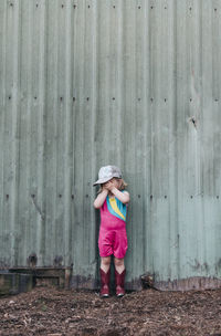 A young girl stands near a barn wearing a leotard and cowgirl boots.