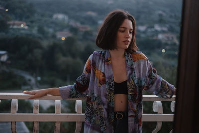 Young woman looking away while standing against railing
