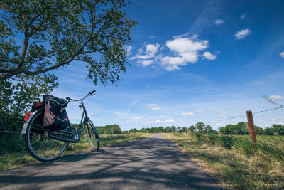 Bicycle on road amidst field against sky