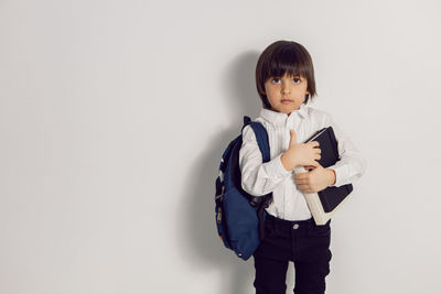 Child boy with a book textbook and backpack stands on a white background