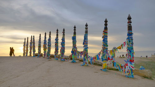 People by multi colored fabric on shaman poles against sky