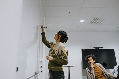 Businessman looking at businesswoman writing strategy on whiteboard in board room