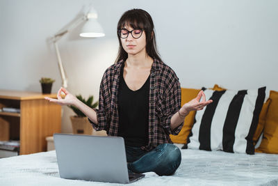 Young woman using smart phone while sitting on laptop
