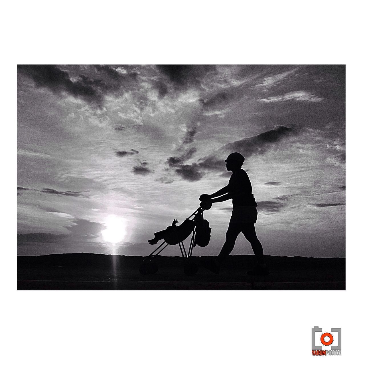 Silhouette person with pram walking on landscape against the sky