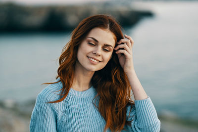 Portrait of beautiful young woman standing against water