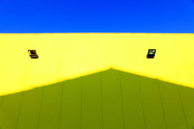 Low angle view of shadow on yellow building against clear blue sky