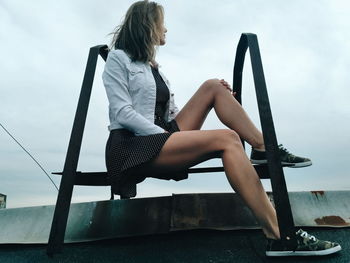 Woman sitting by sea against sky