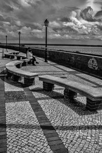 Woman sitting on footpath by street against sky