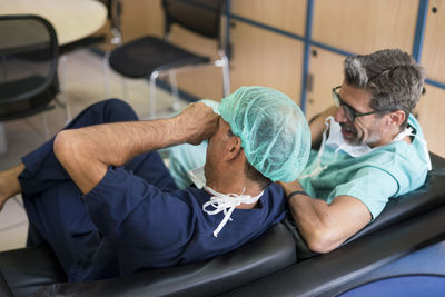 From above shot of two men in surgeon uniform laughing while sitting on comfortable sofa in office