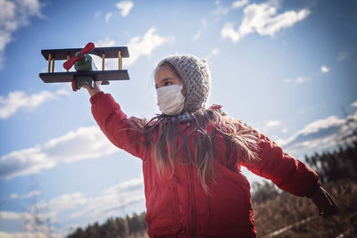 Cute girl wearing respirator mask staying on the meadow with airplane in her hand