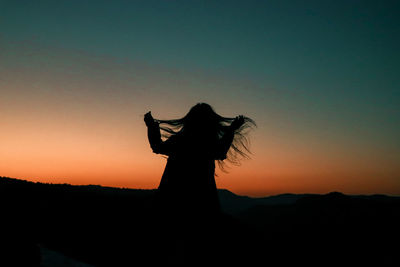 Silhouette woman with arms raised standing against sky during sunset