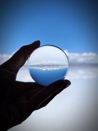 Close-up of hand holding glass against sky