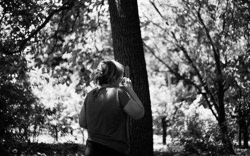 Woman standing and drinking water by tree trunk in forest