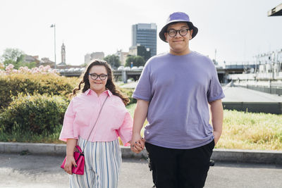 Smiling brother holding hand of sister with down syndrome standing on footpath