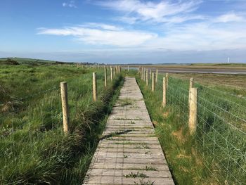 Wooden boardwalk on field against sky