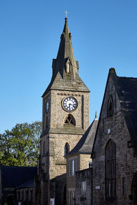 Low angle view of clock tower amidst buildings against clear blue sky