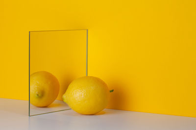 Yellow lemon is reflected in a mirror on a yellow background