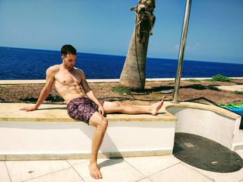 Full length of shirtless man in swimming pool against sea