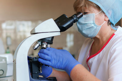 Woman scientist wearing face mask and protective gloves working in laboratory looking