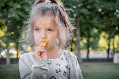 Close-up of cute girl eating food against trees in park