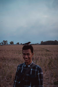 Bird perching smiling young man standing on field