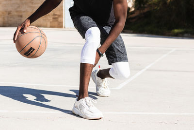 Cropped unrecognizable african american male athlete playing basketball on court in summer and looking at camera