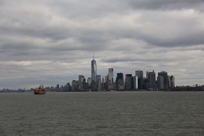 Sea and buildings in city against cloudy sky