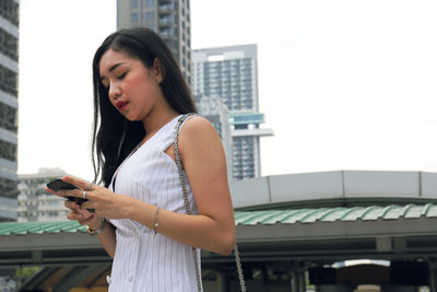 Young woman using mobile phone while standing on office building