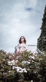 Low angle view of woman looking away while standing by plants against sky