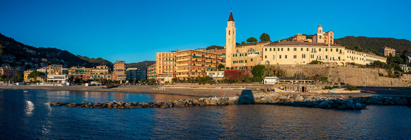Buildings by river against clear blue sky