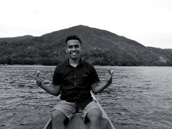 Portrait of young man sitting on mountain against sky