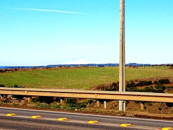 Road by field against clear blue sky