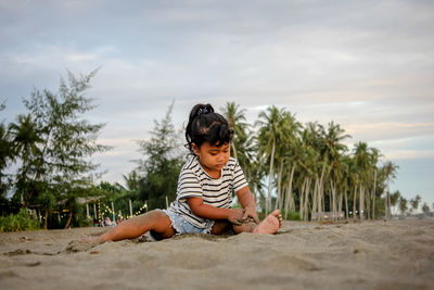 Women sitting on sand at beach against sky