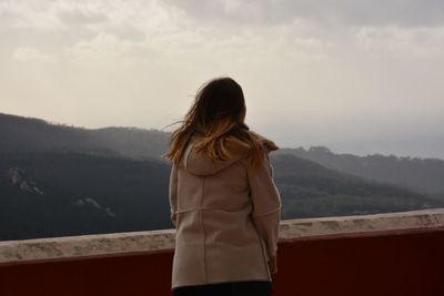 Rear view of woman standing by wall against mountains