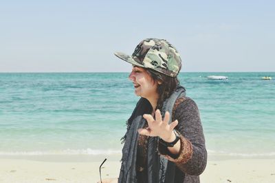 Young woman wearing sunglasses standing at beach against clear sky