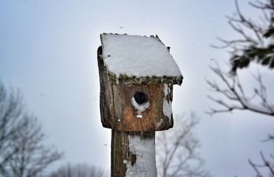 Close-up of birdhouse on snow covered field against sky