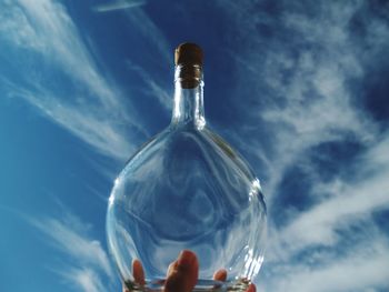 Low angle view of hand holding glass bottle against blue sky