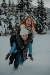 Man carrying woman on back on snow covered land
