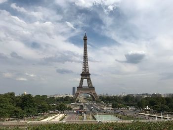 Communications tower in city against cloudy sky